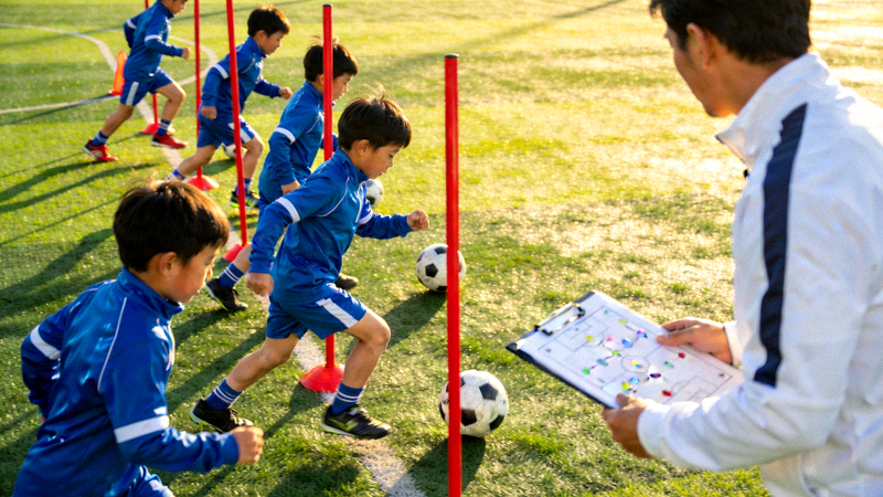 青少年足球训练营小学员在教练指导下进行带球绕杆训练